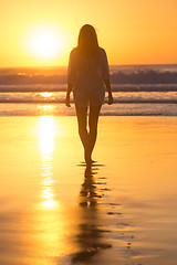 Image showing Lady walking on sandy beach in sunset.