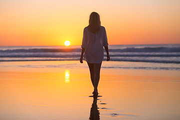 Image showing Lady walking on sandy beach in sunset.