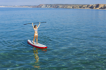 Image showing A beautiful and happy woman with arms up and learning paddle-sur