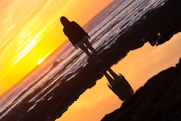 Image showing Woman on rocky beach watching sunset.