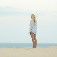 Image showing Woman on sandy beach in white shirt at dusk. 