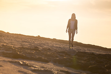 Image showing Woman walking on rocky beach in sunset.