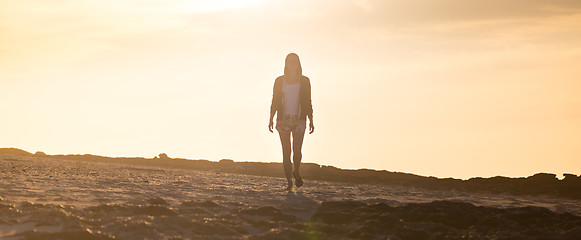 Image showing Woman walking on rocky beach in sunset.