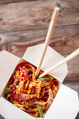 Image showing Noodles with pork and vegetables in take-out box on wooden table