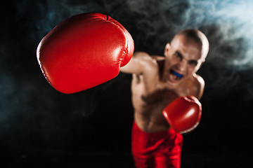 Image showing The young man kickboxing on black  with kapa in mouth