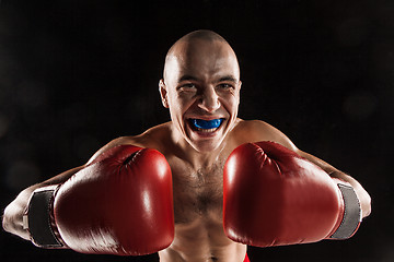 Image showing The young man kickboxing on black  with kapa in mouth