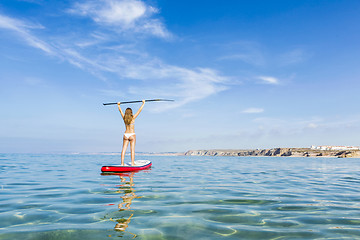 Image showing A beautiful and happy woman with arms up and learning paddle-sur