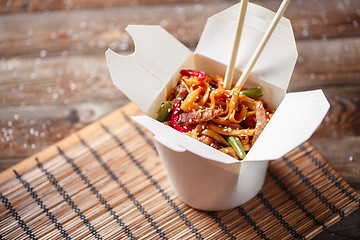 Image showing Noodles with pork and vegetables in take-out box on wooden table