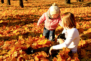 Image showing little sisters play with their cat in the autumn park