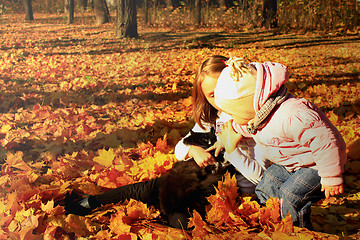 Image showing little sisters play with their cat in the autumn park