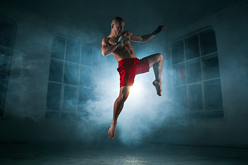 Image showing The young man kickboxing in blue smoke