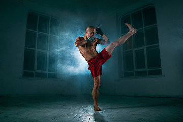 Image showing The young man kickboxing in blue smoke