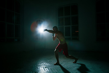 Image showing The young man kickboxing on black background