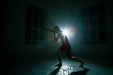 Image showing The young man kickboxing on black background