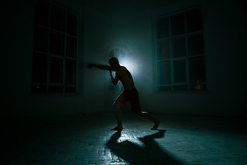 Image showing The young man kickboxing on black background