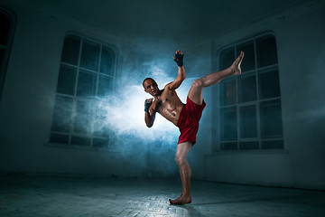 Image showing The young man kickboxing in blue smoke