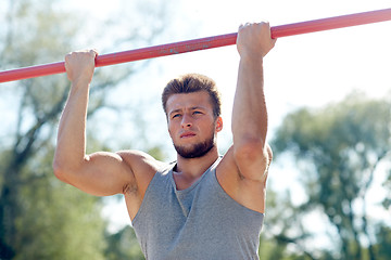 Image showing young man exercising on horizontal bar outdoors