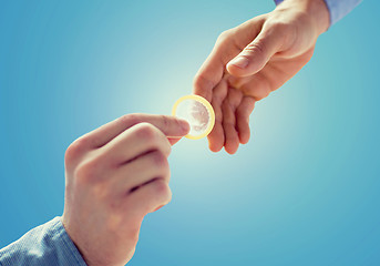 Image showing close up of male gay couple hands giving condom