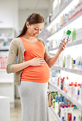 Image showing happy pregnant woman choosing lotion at pharmacy