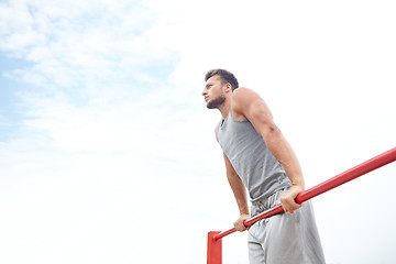 Image showing young man exercising on horizontal bar outdoors