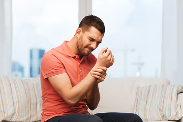 Image showing unhappy man suffering from pain in hand at home