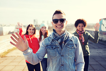 Image showing happy teenage friends waving hands on city street