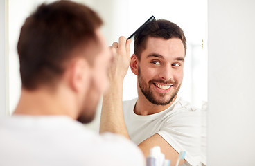 Image showing happy man brushing hair  with comb at bathroom