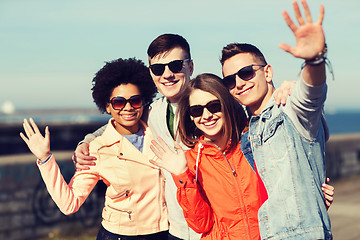 Image showing happy teenage friends in shades waving hands