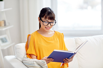 Image showing smiling young asian woman reading book at home