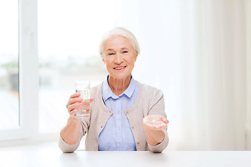 Image showing happy senior woman with water and medicine at home