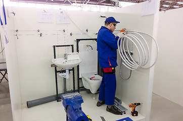 Image showing Young plumber installs equipment for bathroom