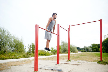 Image showing young man exercising on horizontal bar outdoors