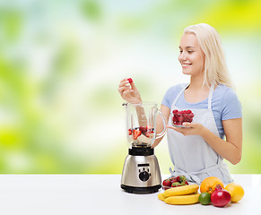 Image showing smiling woman with blender preparing shake at home