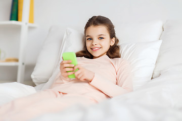 Image showing happy girl lying in bed with smartphone at home