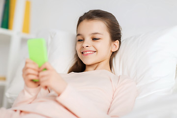 Image showing happy girl lying in bed with smartphone at home