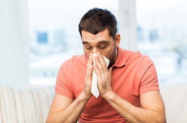 Image showing sick man blowing nose to paper napkin at home