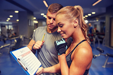 Image showing smiling woman with trainer and clipboard in gym