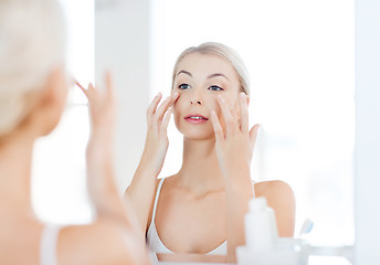 Image showing happy woman applying cream to face at bathroom