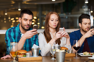 Image showing friends with smartphones dining at restaurant