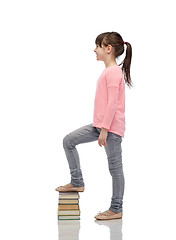 Image showing happy little girl stepping on book pile