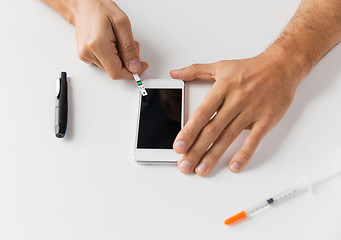 Image showing close up of man with smartphone making blood test