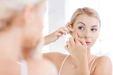 Image showing woman squeezing pimple at bathroom mirror