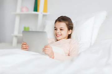 Image showing happy girl lying in bed with tablet pc at home