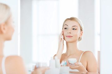 Image showing happy woman applying cream to face at bathroom