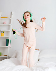 Image showing girl jumping on bed with smartphone and headphones