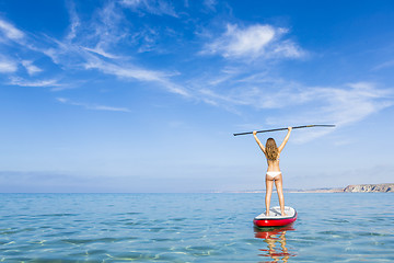 Image showing A beautiful and happy woman with arms up and learning paddle-sur