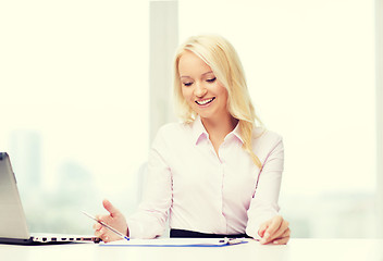 Image showing smiling businesswoman reading papers in office