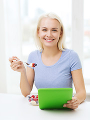 Image showing smiling woman eating fruits with tablet pc at home