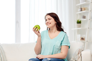 Image showing happy plus size woman eating green apple at home