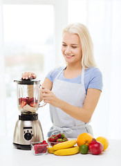 Image showing smiling woman with blender preparing shake at home